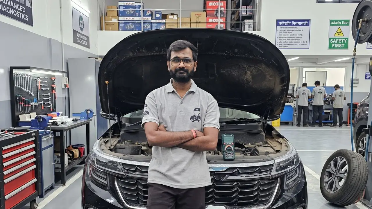 Harish Jaiswal, Garage Gyan trainer, standing in front of a car with the bonnet open in the Car Tool India advanced diagnostics workshop, a multimeter resting on the engine bay